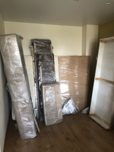 Части мебели аккуратно разобраны, упакованы в пленку и сложены у стены. Видны элементы каркаса, подлокотники и обивка, готовые к транспортировке или хранению.