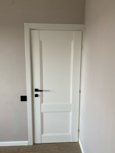 Установлена белая дверь с ручкой и петлями, закреплена коробка, выполнена подгонка, монтаж наличников, проверена функциональность, завершена отделка проема.