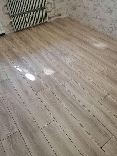 На ровную поверхность уложено покрытие из ламината, создавая гладкий и аккуратный вид. Полосы материала размещены равномерно, обеспечивая эстетичный и современный интерьер.