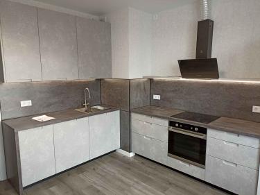 Изображение современной кухни с серыми шкафами и встроенной техникой. На столешнице раковина, плита, вытяжка. Интерьер выполнен в минималистичном стиле с акцентом на функциональность.