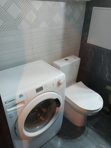 Ванная комната оформлена керамическими плитами: стены декорированы светлыми элементами с геометрическим узором, пол покрыт темными плитками, создавая стильный контраст.