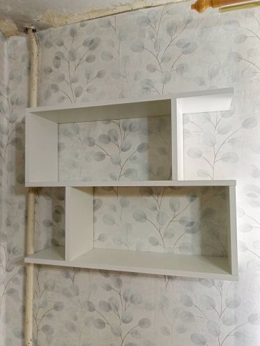 На стене закреплена белая полка сложной формы. Выполнен монтаж с использованием крепежных элементов, обеспечивающих надежность и устойчивость конструкции.