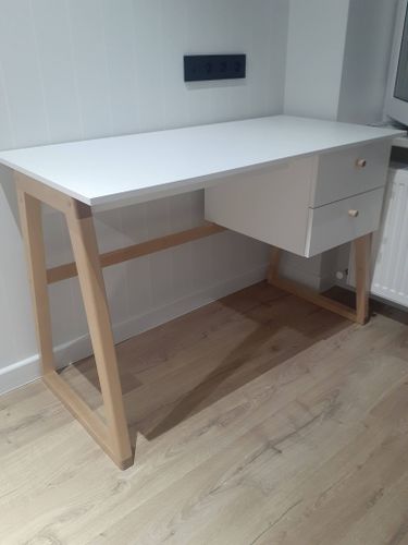 Собран письменный стол: установлены ножки, закреплена столешница, прикручены ящики. Все элементы соединены, конструкция устойчива, готова к использованию.