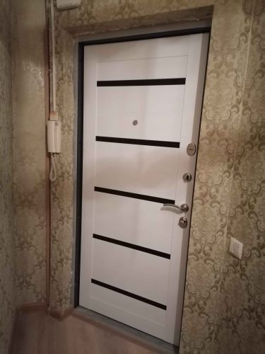 Установлена новая белая дверь с горизонтальными вставками, закреплена в проеме, добавлены ручка и замок, выполнена отделка откосов, обеспечена плотная посадка, проверена функциональность.