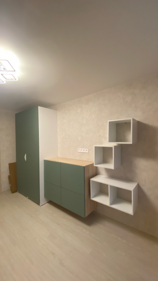 На стене установлена белая полка из четырех секций, образующих геометрическую композицию. Полка надежно закреплена, гармонично вписывается в интерьер, добавляя функциональности и стиля.