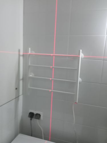 Закреплен электрический полотенцесушитель на стене ванной комнаты. Подключен к электросети через розетку. Установлен с использованием лазерного уровня для точного выравнивания.