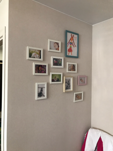 На стене висит коллекция из двенадцати рамок с фотографиями и детским рисунком. Композиция создает уютную атмосферу в комнате.