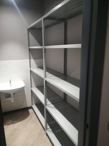 Собран металлический каркас с полками, установлены крепления, обеспечена прочность конструкции. Завершён монтаж в помещении, готов к использованию для хранения.