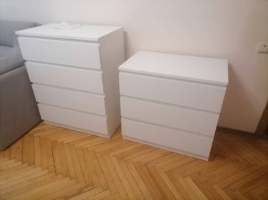 Собраны два белых комода с тремя и четырьмя ящиками, установлены на деревянный пол рядом с диваном. Все детали соединены, ящики выровнены, конструкция устойчива.