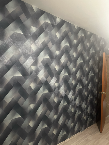 На стену нанесен стеклохолст с геометрическим узором, создающим объемный эффект. Поверхность ровная, без видимых швов, аккуратно обработаны углы и стыки, обеспечивая эстетичный вид.