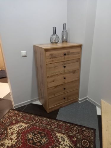 Собран деревянный шкаф с пятью ящиками, установлен в углу комнаты. Все элементы надежно закреплены, фасады выровнены. На верхней поверхности размещены декоративные вазы.