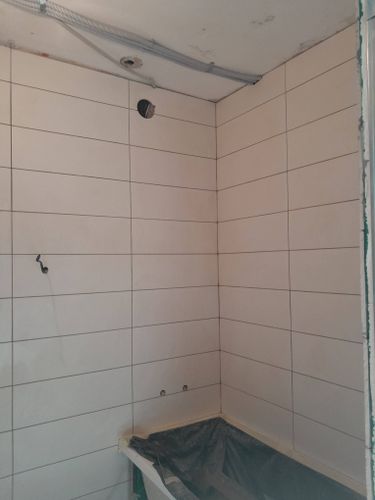 На стенах ванной комнаты ровно уложена светлая керамика. Швы аккуратно заделаны, поверхность подготовлена для дальнейших работ. Углы и стыки оформлены безупречно.