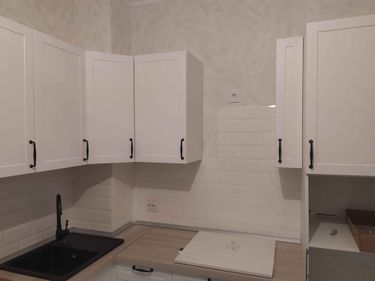 Изготовлены и установлены новые белые дверцы для кухонных шкафов, оснащенные черными ручками. Фасады аккуратно подогнаны под размеры, обеспечивая современный и стильный вид.