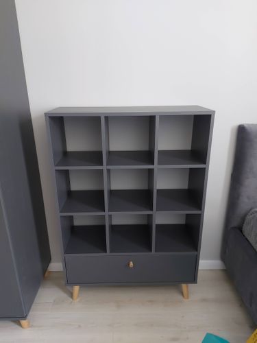 Собран новый стеллаж с девятью ячейками и выдвижным ящиком. Установлены деревянные ножки, обеспечивающие устойчивость. Гладкая поверхность и аккуратные соединения деталей.