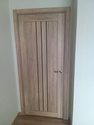 Установлена новая деревянная створка с петлями, ручкой и наличниками. Конструкция выровнена, закреплена в проеме, обеспечена плавная работа. Завершена отделка, проверена функциональность.