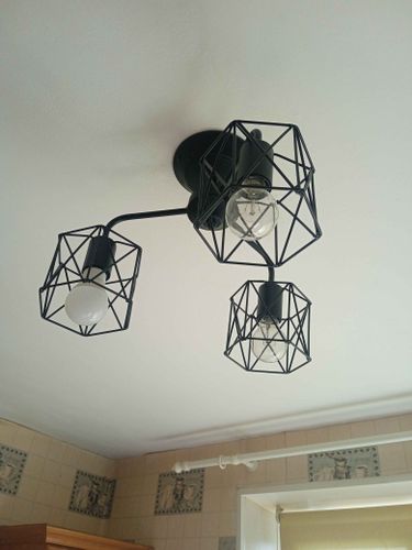 Установлено осветительное устройство с тремя лампами на потолке. Металлическая конструкция крепко зафиксирована, обеспечивая равномерное распределение света в помещении.