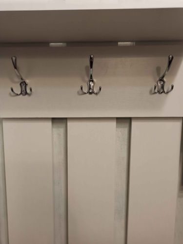 Изображение демонстрирует завершённую установку настенных крючков на деревянной панели. Три металлических держателя аккуратно закреплены, обеспечивая надёжное крепление для одежды или аксессуаров.