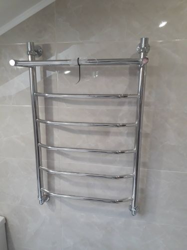 Изображение демонстрирует установленный полотенцесушитель в ванной комнате. Стены облицованы светлой плиткой, создающей аккуратный и современный вид помещения.