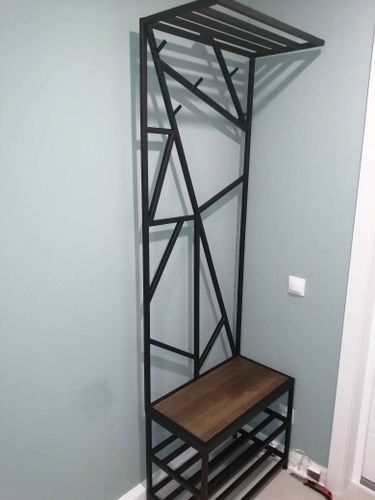 Собрана металлическая конструкция с полкой и крючками для одежды. Установлено сиденье с деревянной поверхностью и нижняя часть для обуви. Все элементы надежно закреплены у стены.