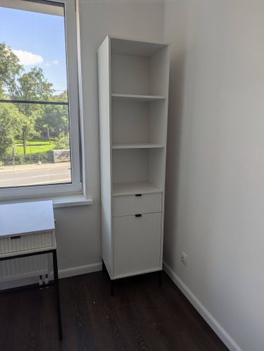 Собрана конструкция с полками и ящиками, установлена в углу комнаты. Белый корпус, черные ножки, аккуратная сборка, надежная фиксация, завершенный вид, готово к использованию.