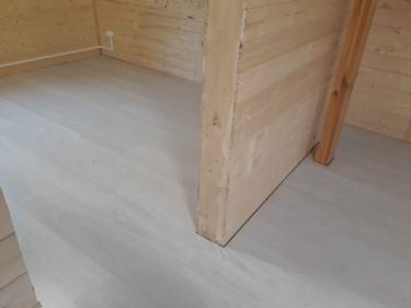 Уложено новое напольное покрытие светлого оттенка в комнате с деревянными стенами. Пол ровный, без зазоров, стыки аккуратные. Работа завершена, помещение готово к использованию.