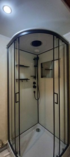 Установлена современная душевая кабина с прозрачными стенками и черной фурнитурой. Поддон белый, оборудован сливом. Смонтированы полки и держатели для удобства.