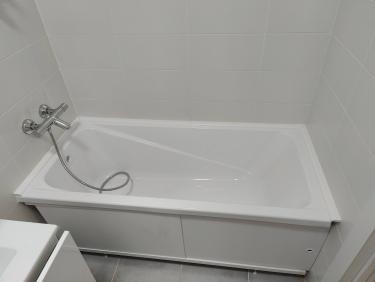 Изображение ванной комнаты с установленной белой ванной, смесителем и душевым шлангом. Стены облицованы плиткой, создавая чистый и современный вид.