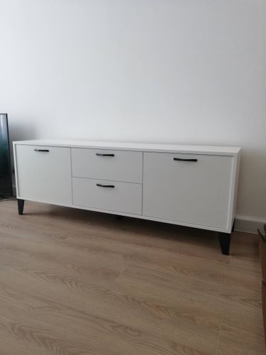 Собрана мебель с тремя выдвижными ящиками и двумя дверцами. Установлены ручки, закреплены ножки, проверена устойчивость и плавность работы механизмов. Готовое изделие размещено на полу.