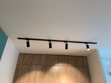 Установлены современные светильники на потолке, обеспечивающие равномерное освещение. Черная трековая система закреплена надежно, лампы направлены для оптимального светораспределения.
