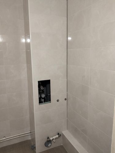 На стенах ванной комнаты уложен светлый керамогранит. Плитка аккуратно выровнена, швы ровные, коммуникации закрыты. Углы и стыки обработаны, поверхность гладкая и чистая.