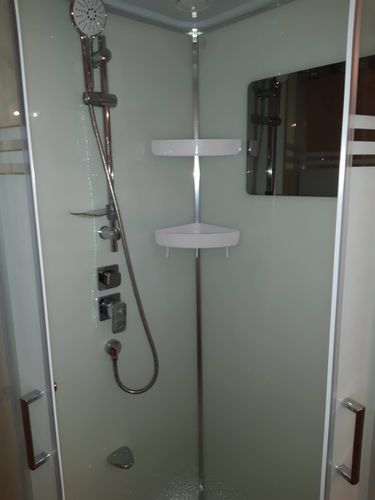 Установлена современная душевая конструкция с низким основанием, закреплены стеклянные панели, подключены смеситель и лейка, герметично зафиксированы соединения, добавлены полки для удобства.