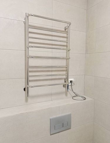 Закреплен полотенцесушитель на стене, подключен к электросети, проверена работоспособность. Устройство надежно установлено, кабель аккуратно размещен, обеспечена безопасность использования.