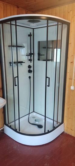Установлена новая душевая кабина с прозрачными стенками и черной фурнитурой. Поддон белого цвета, смеситель и полки закреплены, подключены коммуникации. Стены облицованы панелями.