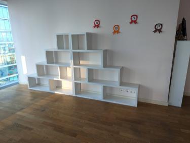 Собран белый модульный шкаф с полками, установлены на деревянный пол у стены. Композиция завершена, элементы выровнены, конструкция устойчива и готова к использованию.