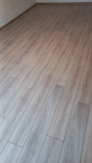 На ровное основание уложено напольное покрытие из ламината, панели подогнаны плотно, швы аккуратные, поверхность гладкая, без зазоров, создаёт единый эстетичный вид.