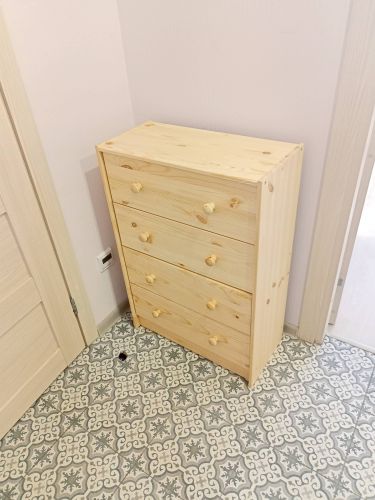 Собран деревянный комод с тремя вместительными ящиками, установлен в углу комнаты. Все детали плотно соединены, ручки прикреплены, конструкция устойчива и готова к использованию.