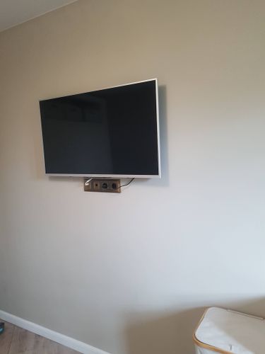 Изображение демонстрирует установленный на стене телевизор с подключенными кабелями и аккуратно закрепленными розетками. Рядом видна часть мебели, создающая уютную атмосферу.