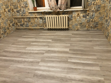 На полу уложено новое покрытие, ровно и аккуратно. Полностью обновлена поверхность, обеспечивая свежий вид и долговечность. Завершено оформление интерьера комнаты.