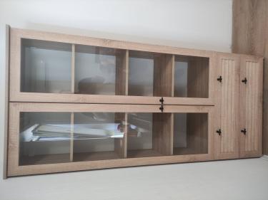 Собран деревянный шкаф с двумя стеклянными дверцами и полками внутри. Установлены ручки и выдвижные ящики. Все элементы надежно закреплены и выровнены.