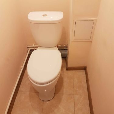 Изображение демонстрирует завершённую установку напольного унитаза, подключенного к системе водоснабжения и канализации. Устройство аккуратно размещено в углу помещения на кафельном полу.