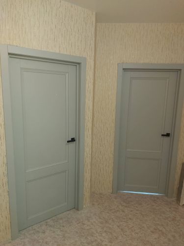 Установлены две одностворчатые двери с серыми полотнами и черными ручками. Дверные коробки надежно закреплены в проемах, обеспечивая плавное открывание и закрывание.