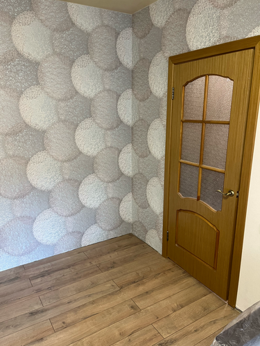 Стены оклеены декоративными полотнами с узором в виде кругов, тщательно выровнены и аккуратно подогнаны по стыкам. Полотно гармонично сочетается с деревянной дверью и полом.