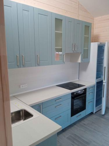 Изображение светлой кухни с голубыми шкафами, встроенной плитой, раковиной и холодильником. Стены отделаны деревом, пол выложен плиткой. Интерьер выглядит современно и аккуратно.