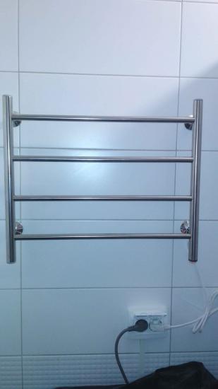 Изображение полотенцесушителя на стене ванной комнаты. Металлическая конструкция с несколькими горизонтальными перекладинами закреплена на плитке. Рядом видна розетка с подключенными проводами.