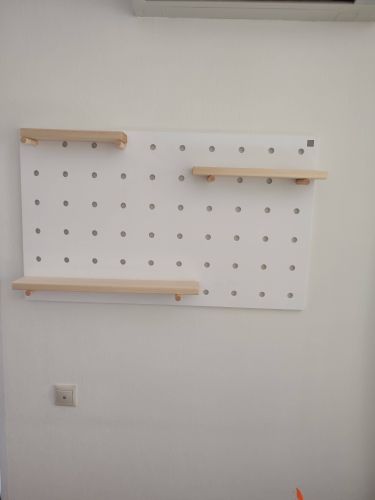 На стену установлен перфорированный щит с тремя деревянными полками. Конструкция надежно закреплена, обеспечивая устойчивость и функциональность для хранения предметов.