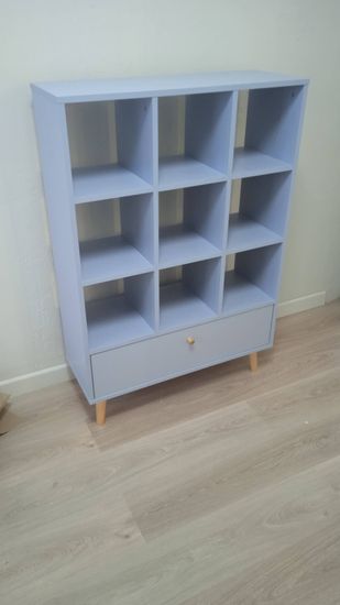 Собран и установлен стеллаж с девятью ячейками и выдвижным ящиком. Устойчиво закреплён на деревянных ножках, готов к использованию.