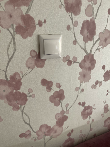 Установлено новое устройство на стене с цветочным узором. Провода подключены, проверена работоспособность. Завершено аккуратно, без повреждений обоев.
