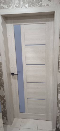 Установлена новая деревянная дверь, закреплена в проеме, добавлены петли, ручка и замок. Полотно ровно выровнено, обеспечена плавная работа, завершена отделка наличниками.