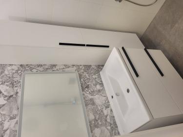 Изображение ванной комнаты с установленной мебелью и сантехникой. Светлые стены, современный умывальник с ящиками, зеркало, шкаф и душевая зона.