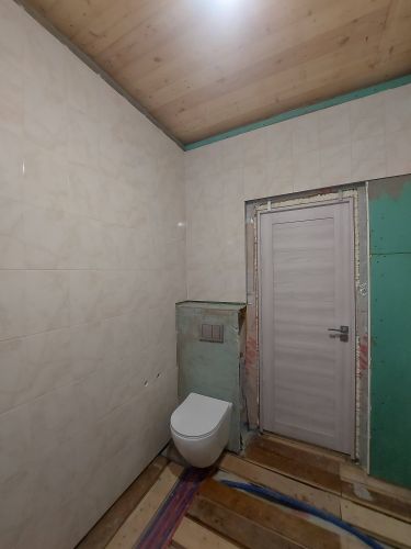 Отделка стен керамическими плитами завершена. Установлен подвесной унитаз. Подготовлены поверхности, уложены элементы ровно, швы аккуратно заделаны. Потолок деревянный.